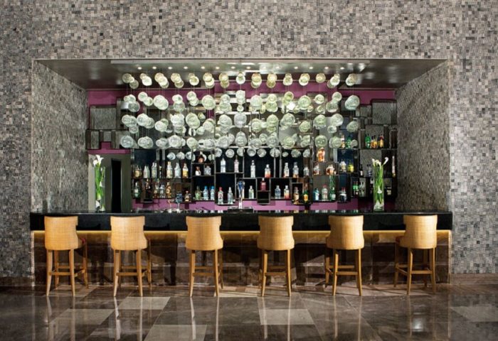 Bar at Secrets Vallarta Bay Resort, an all-inclusive, adults-only, gay-friendly hotel. Interior design with bottles and stools.