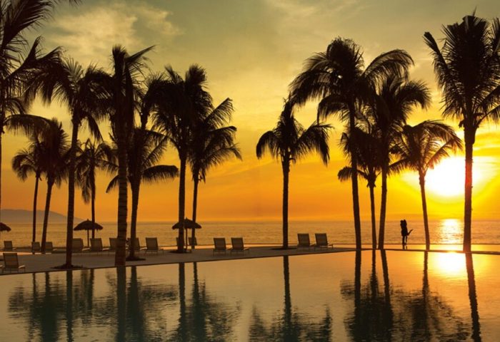 Secrets Vallarta Bay Resort all-inclusive adults-only gay-friendly hotel at sunset. Palm trees, pool, ocean view. Romantic travel.