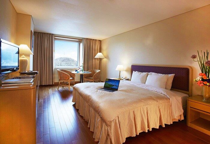 Sejong Hotel Seoul Myeongdong room. Gay-friendly hotel bedroom with laptop on bed, window view, desk, and seating area. Seoul travel.
