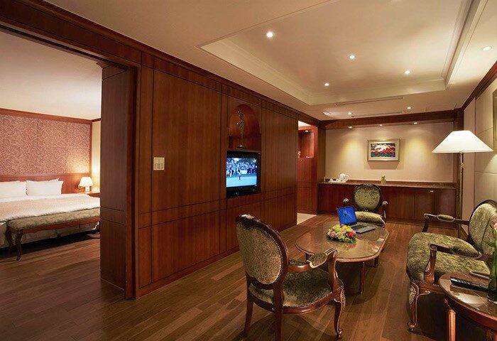 Sejong Hotel Seoul Myeongdong gay-friendly room. Living area with TV, chairs, and table. Bedroom visible through doorway. Luxury stay.