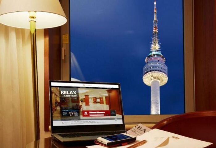 Sejong Hotel Seoul Myeongdong room view of Seoul Tower at night. Gay-friendly hotel with laptop, phone, and papers on the desk.