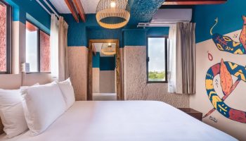Selina Cancun Laguna Hotel Zone gay-friendly room. Bed with white sheets, colorful snake mural, and a view. Perfect for gay travel in Cancun.