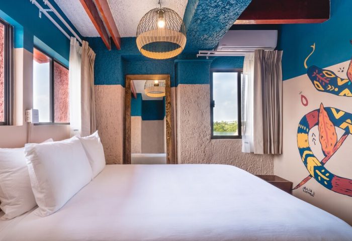 Selina Cancun Laguna Hotel Zone gay-friendly room. Bed with white sheets, colorful snake mural, and a view. Perfect for gay travel in Cancun.
