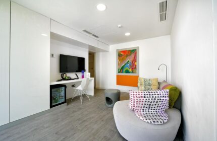 Seven Hotel & Wellness room. Gay men only hotel featuring modern decor, TV, mini fridge, seating area, and colorful abstract art.
