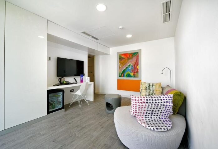 Seven Hotel & Wellness room. Gay men only hotel featuring modern decor, TV, mini fridge, seating area, and colorful abstract art.