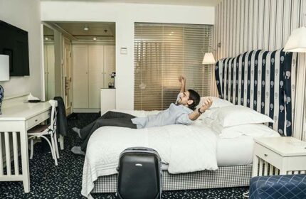 Gay-friendly Shalom Hotel & Relax, an Atlas Boutique Hotel. Man relaxing on bed in pet-friendly room. Suitcase. Gay men travel advice.