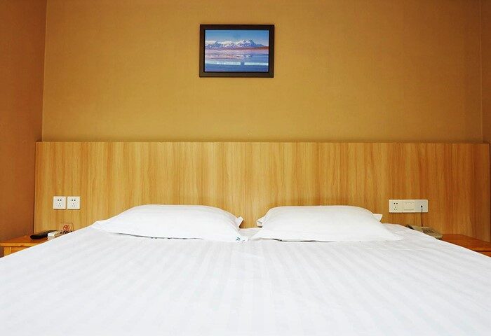 Room at Shanghai Blue Mountain Youth Hostel Luwan, a gay-friendly hotel. Double bed with white linens and a picture on the mustard-colored wall.