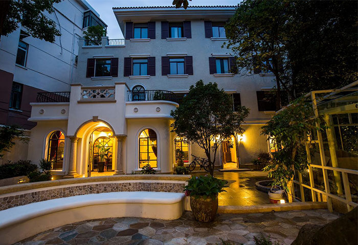 Shanghai Soho Garden Hotel exterior at dusk. Gay-friendly hotel with arched windows, stone patio, and inviting atmosphere. A great choice for gay travel.
