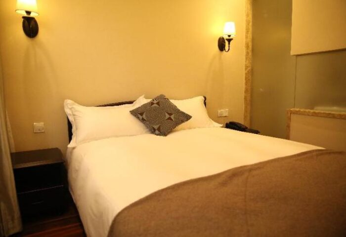 Bedroom at Shanghai Soho Garden Hotel, a gay-friendly hotel. Bed with white sheets and brown blanket, bedside table, and wall-mounted lamps.