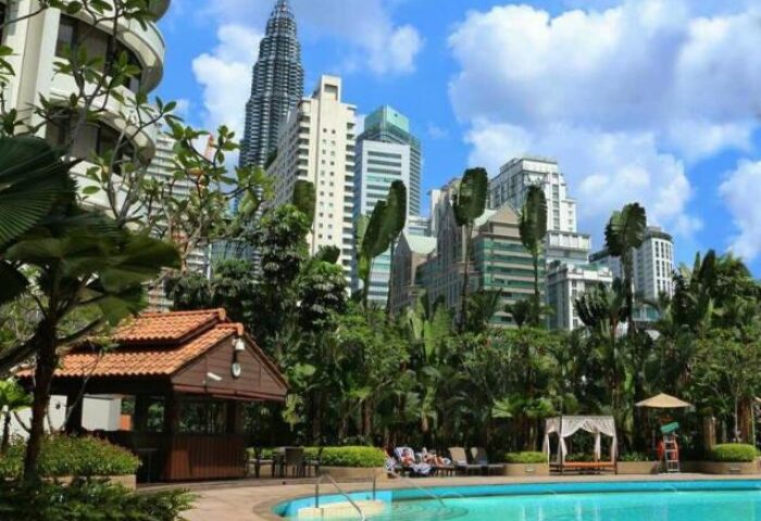 Shangri-La Hotel Kuala Lumpur pool view. Gay-friendly hotel with city skyline. Lush greenery, pool, and Petronas Towers in the background.