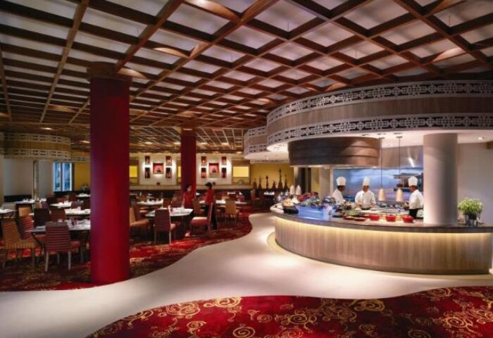 Shangri-La's Rasa Sentosa Resort & Spa restaurant. Chefs at the counter, tables set, red patterned carpet. Gay-friendly hotel dining.
