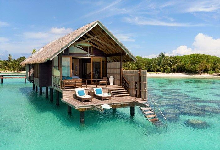 Shangri-La's Villingili Resort & Spa overwater bungalow. Gay-friendly hotel with deck chairs and stairs into turquoise water. Tropical beach.