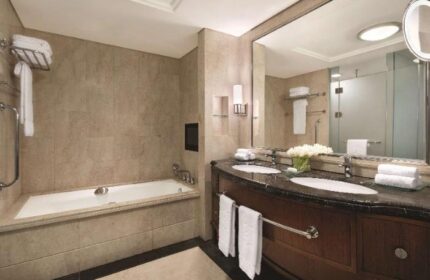 Bathroom at Shangri-La Hotel Jakarta, a gay-friendly hotel. Features a bathtub, double vanity with marble countertop, and a large mirror.