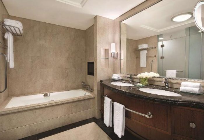 Bathroom at Shangri-La Hotel Jakarta, a gay-friendly hotel. Features a bathtub, double vanity with marble countertop, and a large mirror.