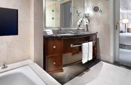 Bathroom interior at Shangri-La Hotel Jakarta, a gay-friendly hotel. Features a vanity with towels, a mirror, and a glimpse into the bedroom.