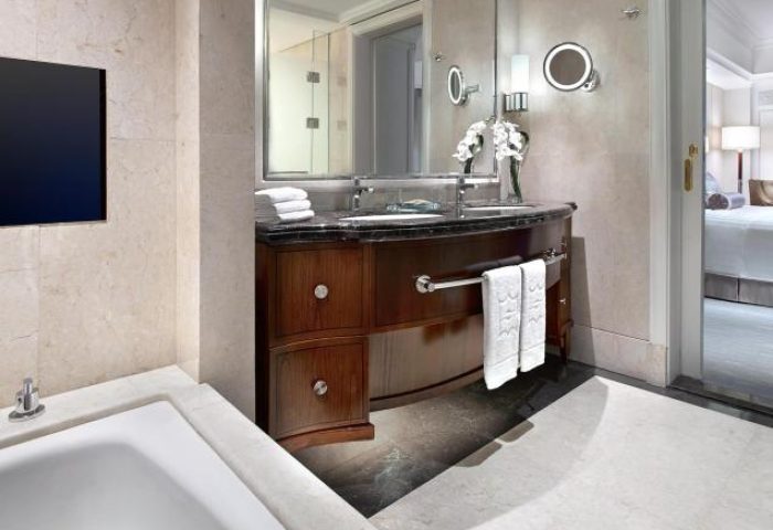 Bathroom interior at Shangri-La Hotel Jakarta, a gay-friendly hotel. Features a vanity with towels, a mirror, and a glimpse into the bedroom.
