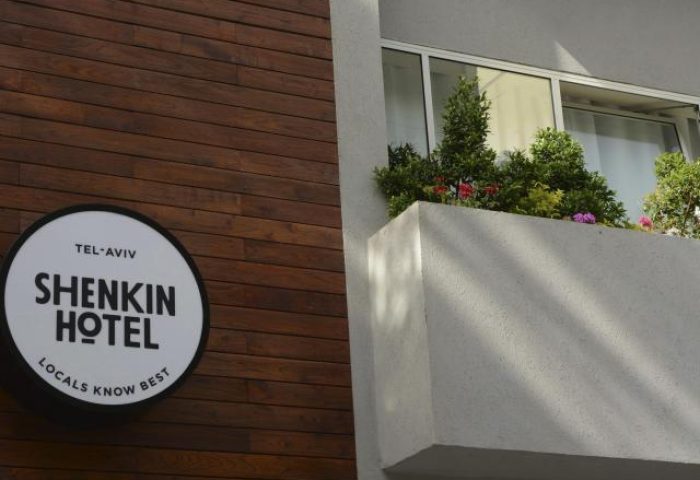 Shenkin Hotel, a gay-friendly hotel in Tel Aviv. Exterior view with the hotel's sign on a wooden wall and a balcony with plants and flowers.