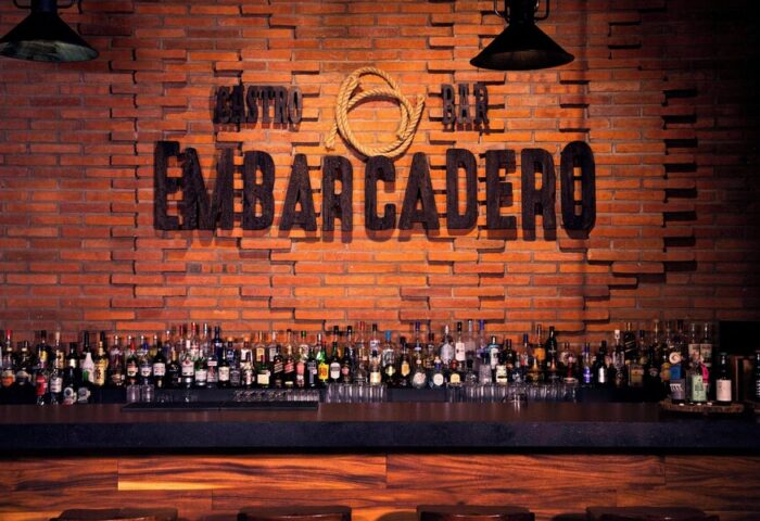 Bar at Sheraton Buganvilias Resort, a gay-friendly hotel. Embarcadero sign on brick wall, bottles on the bar. Great drinks await!