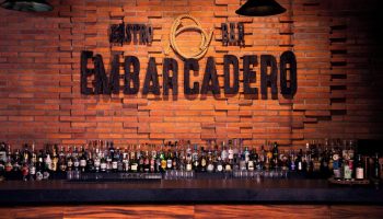 Bar at Sheraton Buganvilias Resort, a gay-friendly hotel. Embarcadero sign on brick wall, bottles on the bar. Great drinks await!