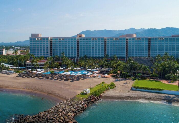 Gay-friendly Sheraton Buganvilias Resort and Convention Center aerial view. Beachfront hotel with pools, palm trees, and mountains in the background.