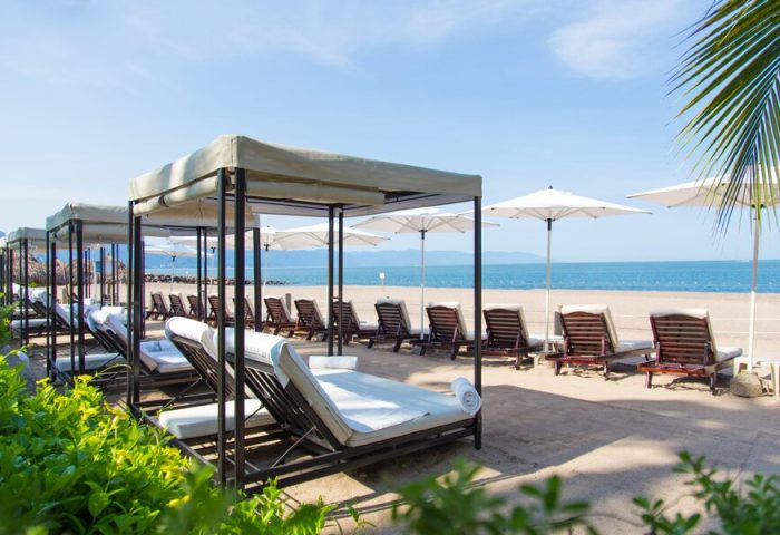 Beach at Sheraton Buganvilias Resort, a gay-friendly hotel. Lounge chairs with canopies and umbrellas on the sand near the ocean.