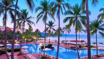 Sheraton Buganvilias Resort pool at dusk. Gay-friendly hotel with palm trees, lounge chairs, and ocean view. Perfect for gay travel.