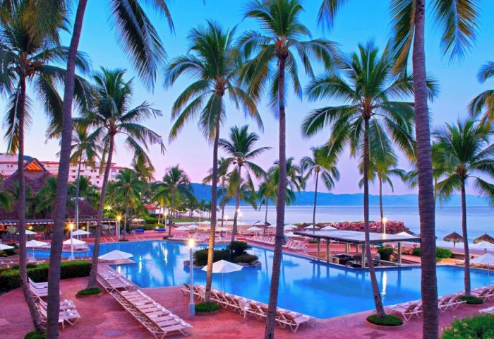 Sheraton Buganvilias Resort pool at dusk. Gay-friendly hotel with palm trees, lounge chairs, and ocean view. Perfect for gay travel.