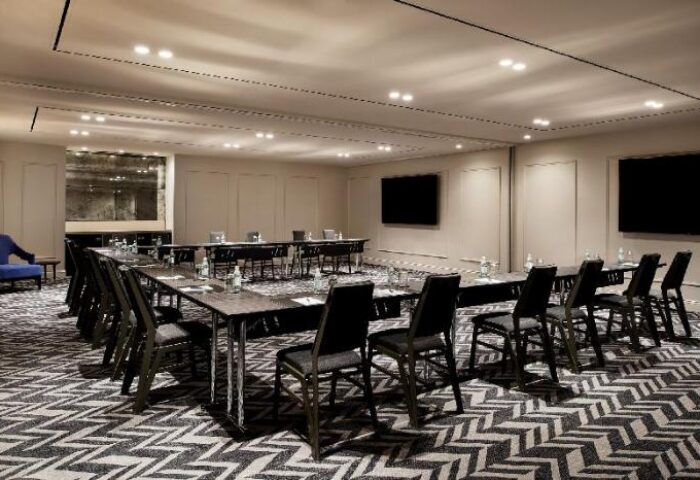 Sheraton Grand Sydney Hyde Park meeting room. Gay-friendly hotel with tables, chairs, and screens for events. Modern business space.