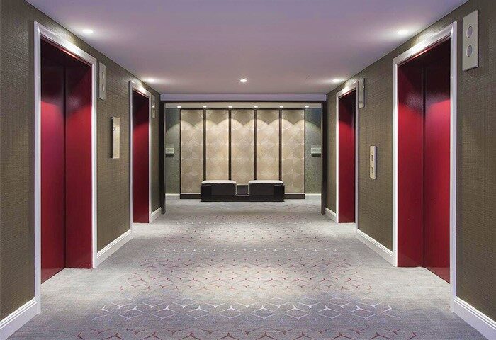 Hallway with red elevators at Sheraton Grand Sydney Hyde Park, a gay-friendly hotel. Interior design with modern accents.