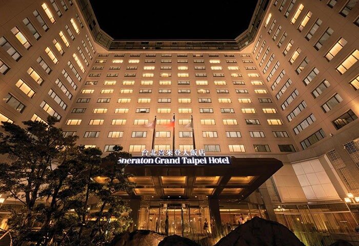 Sheraton Grand Taipei Hotel exterior at night. A gay-friendly hotel in Taipei, Taiwan, with illuminated windows and flags.