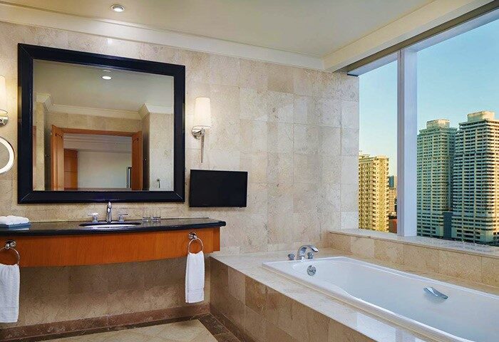Bathroom at Gay-Friendly Sheraton Manila Bay Hotel. Features a tub with a city view, a large mirror, and modern fixtures. Luxury travel.