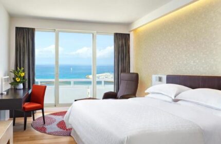 Sheraton Tel Aviv Hotel bedroom with sea view. Gay-friendly, pet-friendly hotel. Room with desk, chair, and balcony overlooking the Mediterranean.