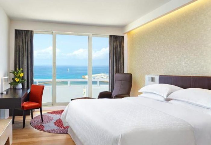 Sheraton Tel Aviv Hotel bedroom with sea view. Gay-friendly, pet-friendly hotel. Room with desk, chair, and balcony overlooking the Mediterranean.