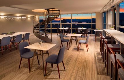 Sheraton Vancouver Wall Centre's stylish lounge with spiral staircase, tables, and city views. Gay-friendly hotel with modern design.