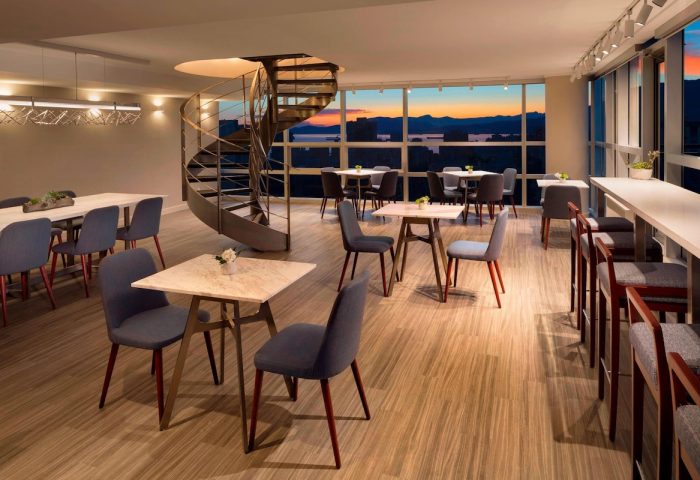 Sheraton Vancouver Wall Centre's stylish lounge with spiral staircase, tables, and city views. Gay-friendly hotel with modern design.
