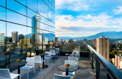 Rooftop patio at the gay-friendly Sheraton Vancouver Wall Centre hotel. City and mountain views, tables, chairs, and glass facade reflecting the skyline.