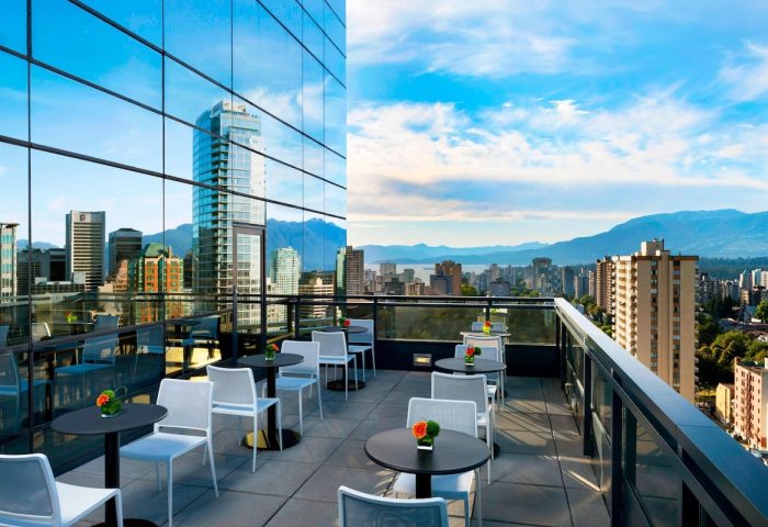 Rooftop patio at the gay-friendly Sheraton Vancouver Wall Centre hotel. City and mountain views, tables, chairs, and glass facade reflecting the skyline.