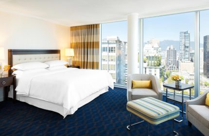 Gay-friendly Sheraton Vancouver Wall Centre hotel room. City view from window. Comfortable bed, chairs, and modern decor. Ideal for gay travel.