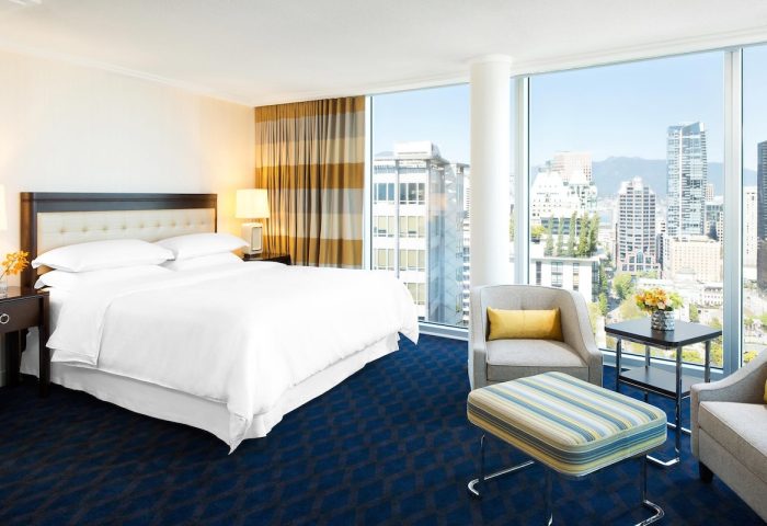 Gay-friendly Sheraton Vancouver Wall Centre hotel room. City view from window. Comfortable bed, chairs, and modern decor. Ideal for gay travel.