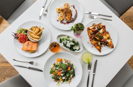 Fine dining at gay-friendly Sheraton Vancouver Wall Centre. Salmon, fries, pizza, salad, and drinks on a white table. Hotel restaurant.