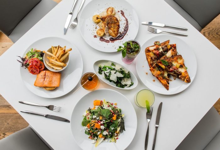Fine dining at gay-friendly Sheraton Vancouver Wall Centre. Salmon, fries, pizza, salad, and drinks on a white table. Hotel restaurant.