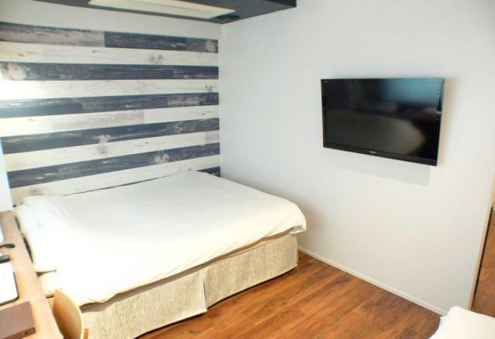 Room at Shinjuku City Hotel N.U.T.S Tokyo, a gay-friendly hotel. Bed with wood-style headboard, TV, and hardwood floors. Modern design.