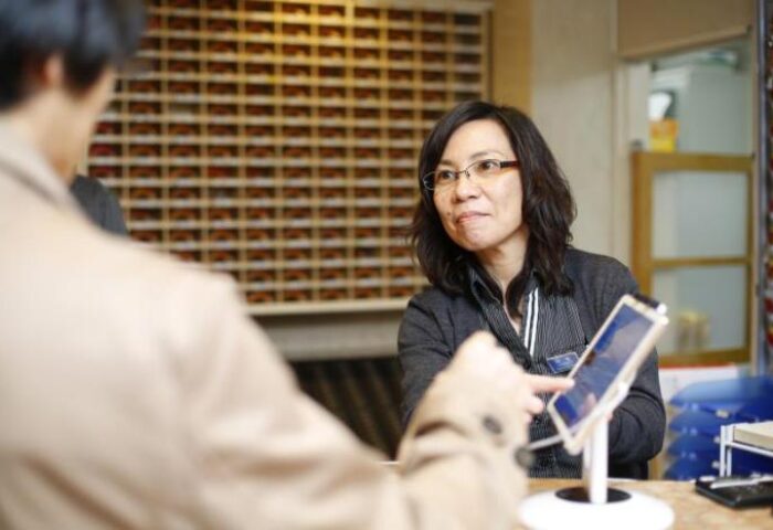 Reception at Shinjuku Kuyakusho-mae Capsule Hotel, a gay-friendly option. Staff assists a guest, showcasing the hotel's capsule rooms.