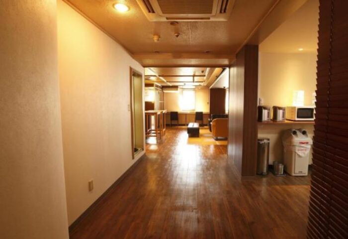 Interior of Shinjuku Kuyakusho-mae Capsule Hotel, a gay-friendly hotel. Hallway with wooden floors, shared kitchen, and workspace. Japan travel.