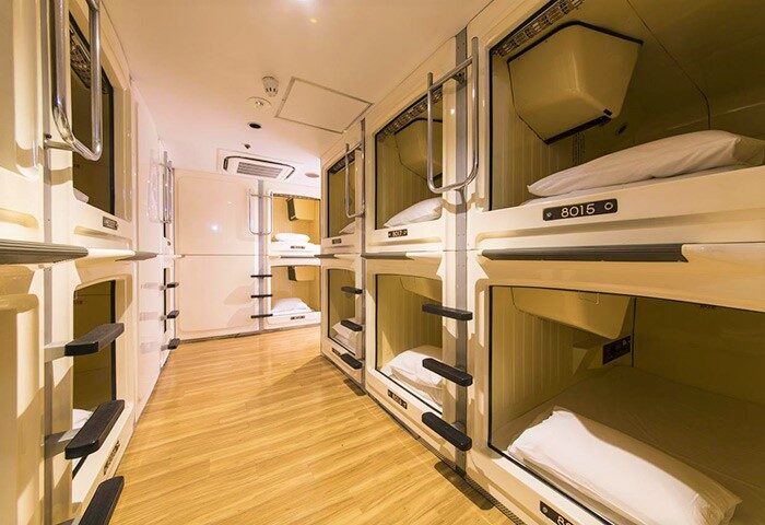 Interior of Shinjuku Kuyakusho-mae Capsule Hotel, a gay-friendly pod hotel. Rows of sleeping capsules with ladders and bedding are visible.