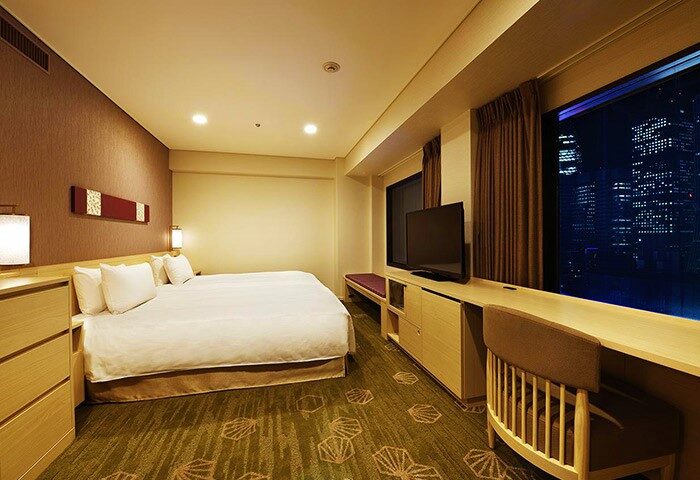 Shinjuku Prince Hotel room at night. Gay-friendly hotel with city view. Modern interior, bed, TV, and desk. Ideal for gay travel in Tokyo.