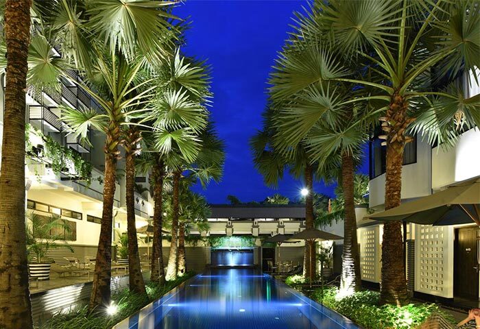 Shinta Mani Angkor's pool villas at night. Gay-friendly hotel with palm trees, blue pool, and modern design. Bensley Collection for gay travel.