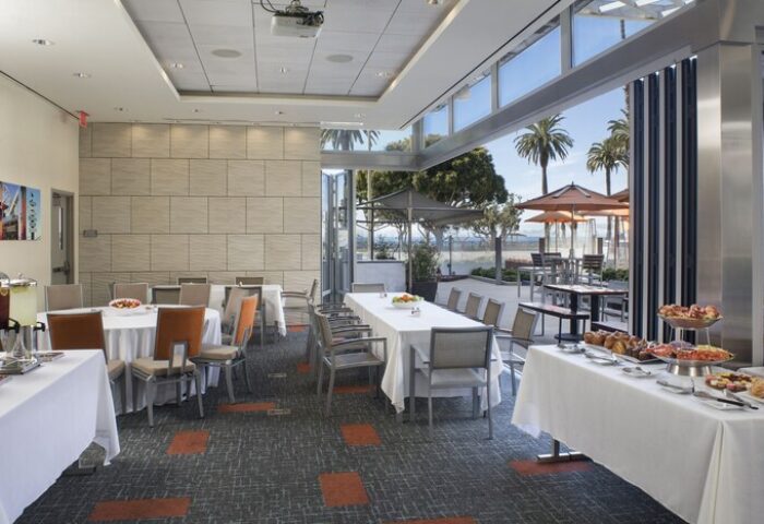 Shore Hotel's event space with tables, chairs, and buffet. Open doors lead to an outdoor patio with palm trees. Gay-friendly hotel.
