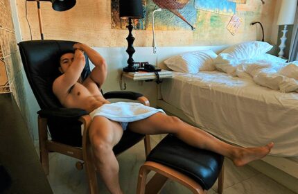 Gay-friendly Siam @ Siam Design Hotel Bangkok: A shirtless man lounges in a chair, towel-clad, in a stylish room. Gay travel luxury.