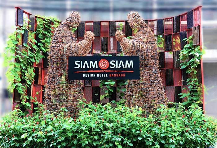 Siam @ Siam Design Hotel Bangkok entrance. Gay-friendly hotel with unique design. Two statues flank the hotel's sign, surrounded by lush greenery.